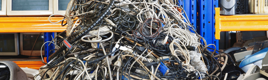 A large, tangled pile of mixed computer cables, power cords, and electronic wiring scrap at an e-waste recycling warehouse.