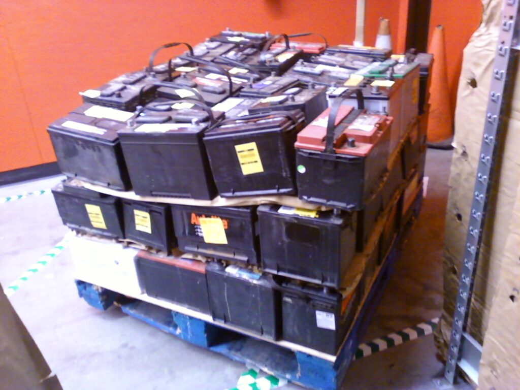 Dozens of used car and truck core batteries neatly stacked on a blue wooden pallet for core return or recycling.